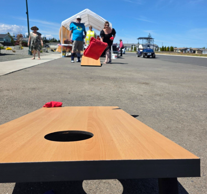 A low-angle, action shot of a cornhole game being played outdoors on an asphalt surface under a bright blue sky