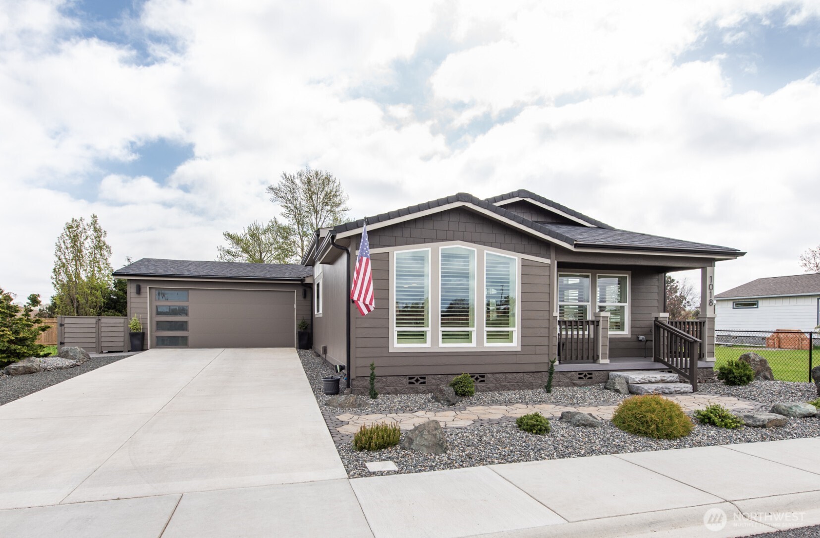 A single-story, modern craftsman-style house with dark brown and beige siding under a cloudy sky